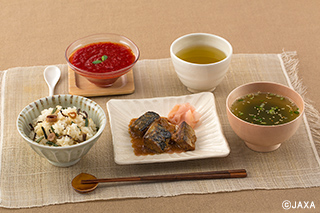 現在の宇宙日本食28品目から作られた献立の一例。 手前左から山菜おこわ、サバの味噌煮、わかめスープ。奥左から野菜飲料ゼリー（トマト）、緑茶。食のバラエティ、特に不足していた野菜類のメニューを増やすことが課題だった。（提供：JAXA） 
