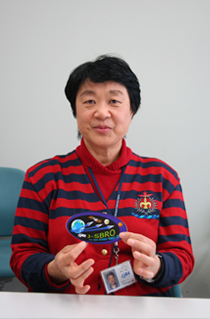 向井千秋さん。1994年7月、アジア人女性で初めて宇宙飛行し、82テーマの実験を実施。1998年10月に2度目の宇宙飛行を行う。2007年10月からJAXA宇宙医学生物学研究室室長に。手にしているのは同研究室のロゴマーク。
