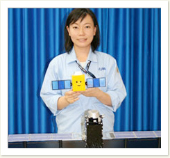 「みちびきさん」を手にする明神絵里花さん。2003年入社。高知県出身で九州大学での専攻は航空工学。高校1年生の時にホーキング博士の本で宇宙に興味を持った。切れ長の目が素敵なカッコいい女性です。