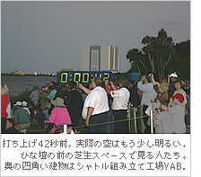 打ち上げ42秒前。実際の空はもう少し明るい。ひな壇の前の芝生スペースで見る人たち。奥の四角い建物はシャトル組み立て工場VAB．